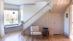 A room with a wooden floor, a white chair, a staircase, and a window with a view of the outside. - Hale House, Customizable Historic Gem in downtown Bayfield (Bayfield)