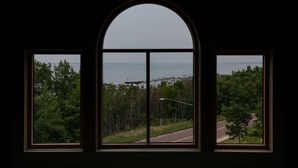 A view through a window with a curved top, overlooking a road, trees, and a body of water with boats. - Hale House, Customizable Historic Gem in downtown Bayfield (Bayfield)