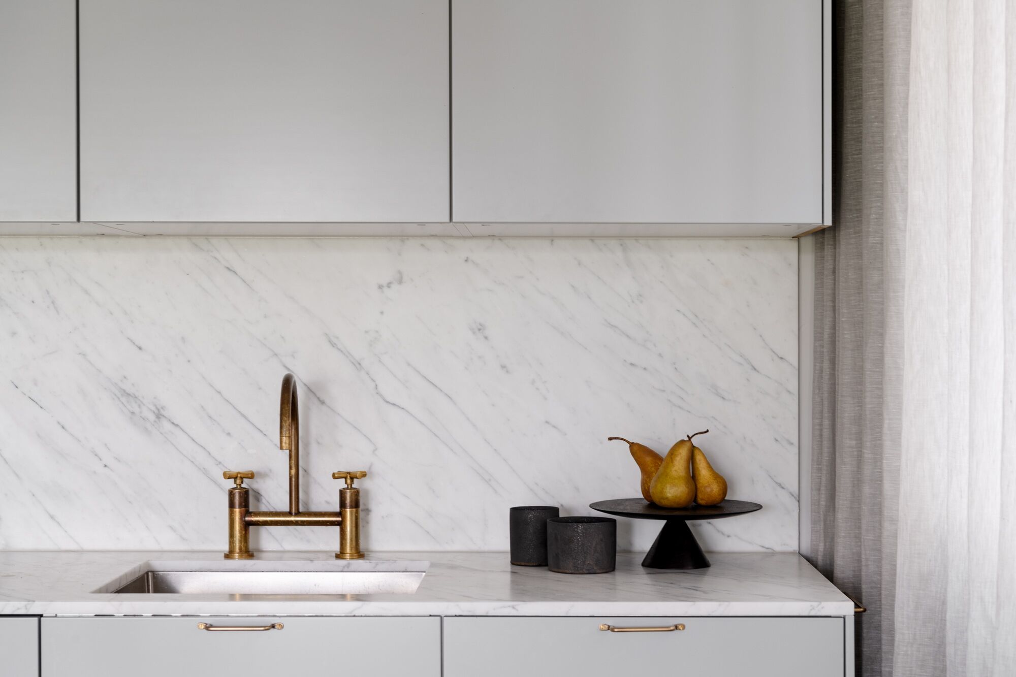 A kitchen with a marble countertop, gold faucets, and a fruit bowl.