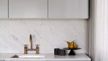 A kitchen with a marble countertop, gold faucets, and a fruit bowl.