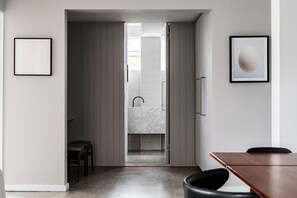 A modern interior with a kitchen area, a dining table, and a view into a bathroom. - Prestigious in Prahran by Ready Set Stay- linen, WIFI, across the road from park (Prahran)