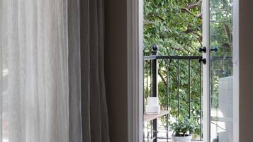 A view through a window with sheer curtains, a metal railing, a potted plant, and a white table.