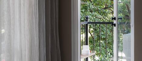 A view through a window with sheer curtains, a metal railing, a potted plant, and a white table.