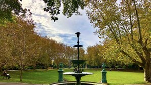 Ein Brunnen in einem Park mit metallenen, grünlichen Strukturen und einer kreisförmigen Becken.
