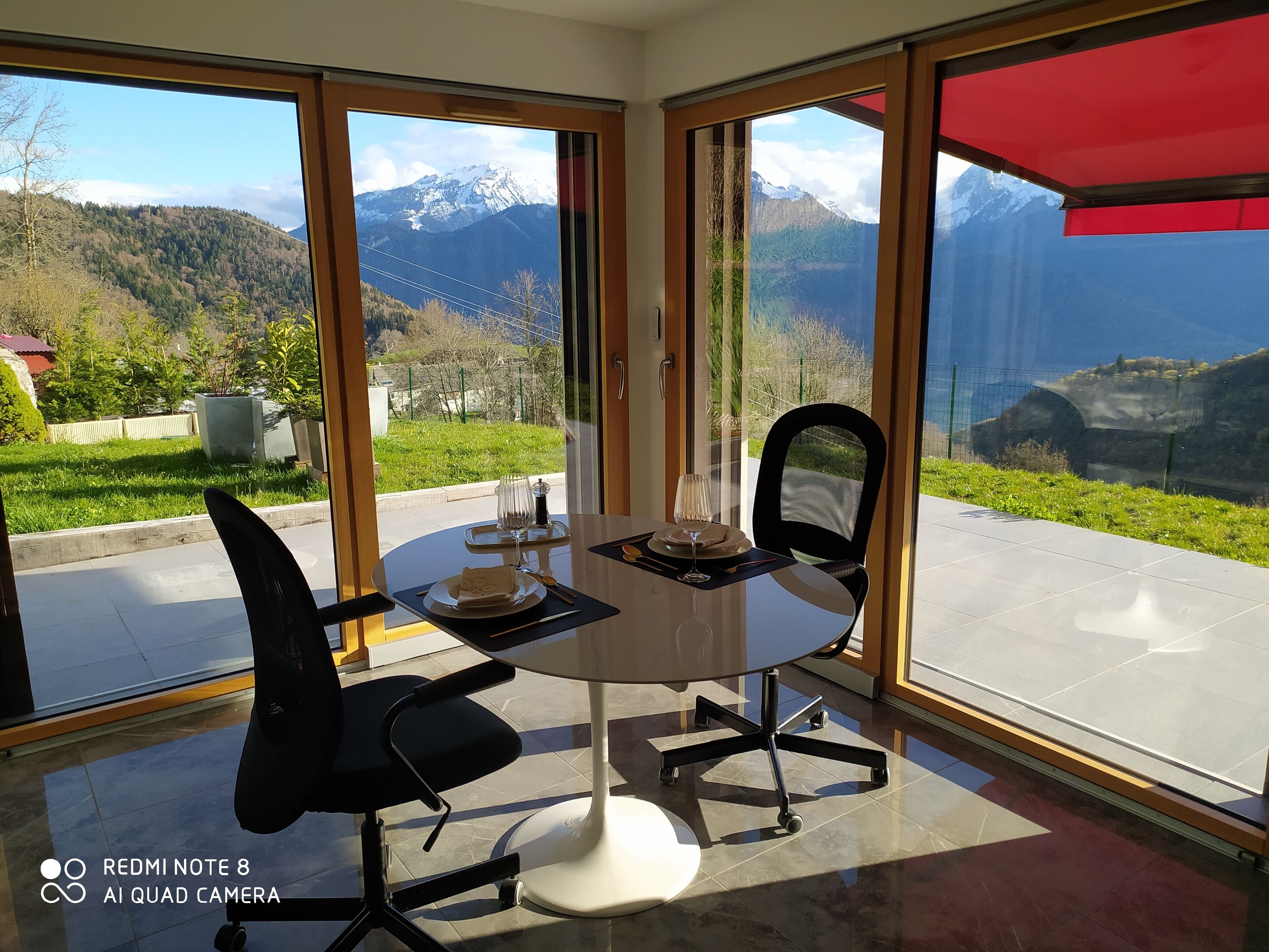 A dining area with a table set for two, large windows offering a mountain view, and a red awning.