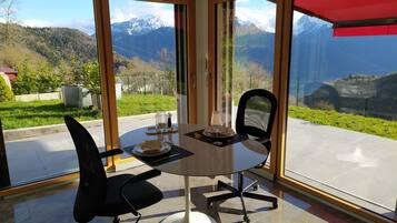 A dining area with a table set for two, large windows offering a mountain view, and a red awning.