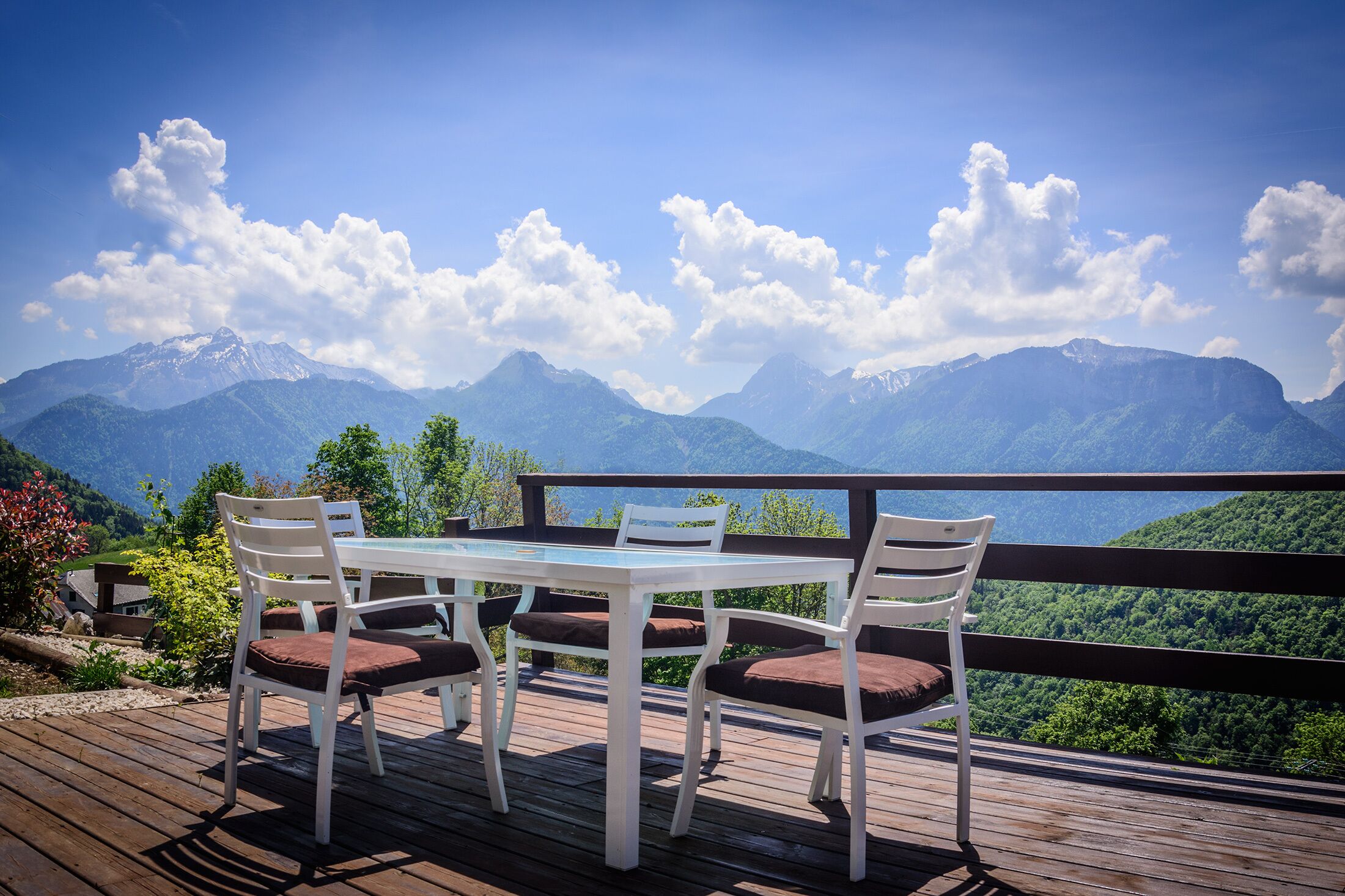 A wooden deck with a table and chairs overlooking a mountainous landscape.