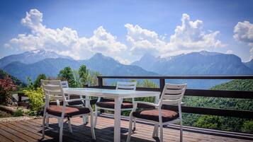 A wooden deck with a table and chairs overlooking a mountainous landscape.
