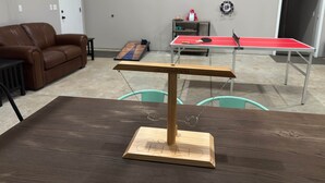 Um quarto com uma mesa de pingue-pongue, uma mesa de madeira com suporte metálico, um sofá de couro marrom e uma porta.