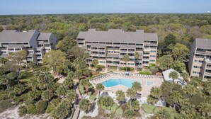 A multi-story hotel with a central courtyard featuring a swimming pool, surrounded by lush greenery and palm trees.