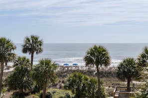 A beach view with palm trees and a wooden deck. - Oceanfront Bliss: 2BR/3rd Floor Condo with Pool & Beach Access in Palmetto Dunes (Hilton Head Island)