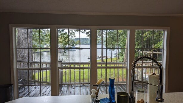 A room with a large window overlooking a lake, a wooden deck, and outdoor furniture.