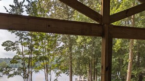 A covered outdoor seating area with a glass table and chairs, overlooking a lake and dock.