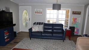A living room with a blue leather sofa, a wooden coffee table, a television on a stand, and a bookshelf.