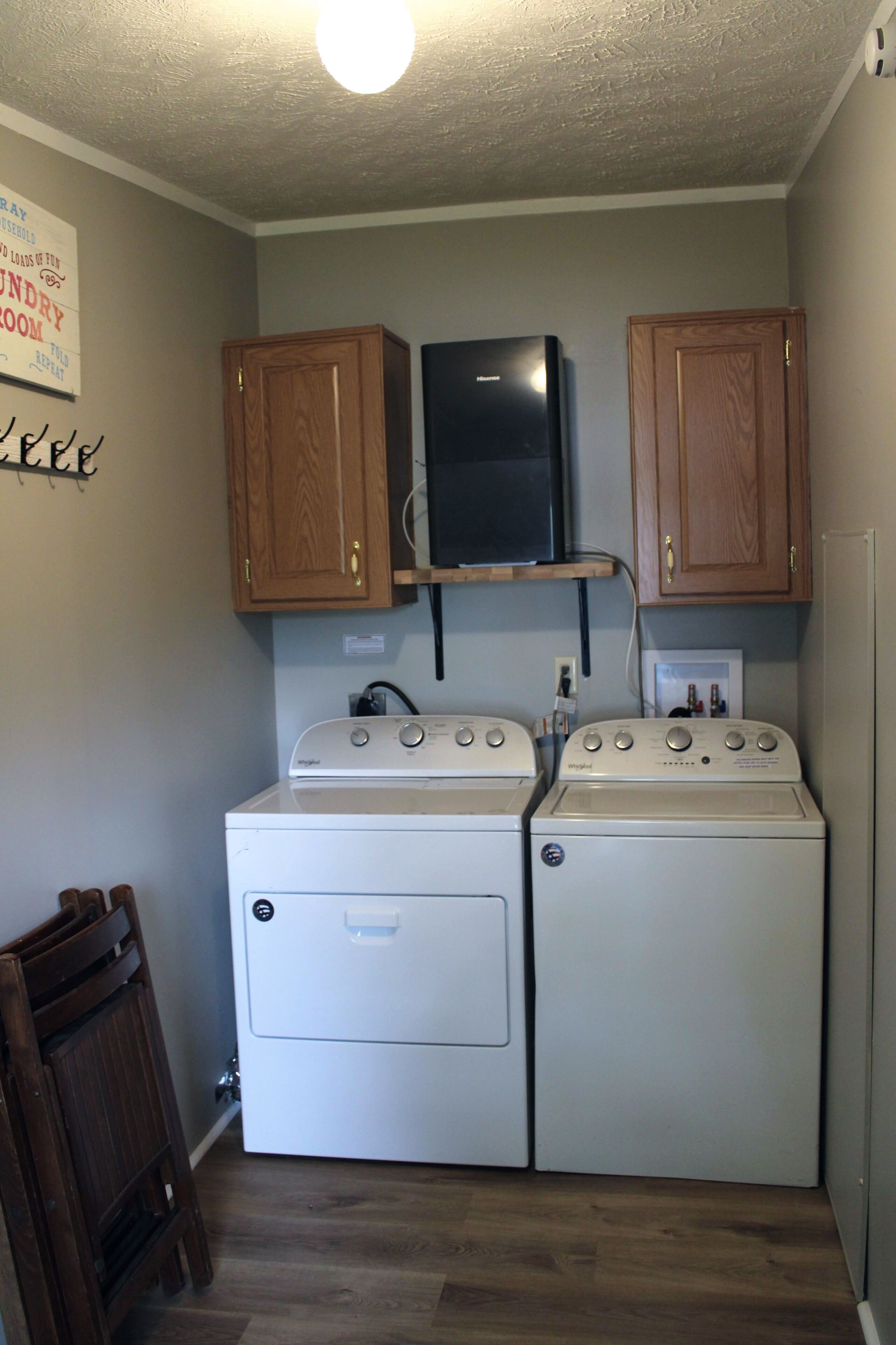 A laundry room with two stacked washers and dryers, wooden cabinets, a black television, and a light fixture on the ceiling.