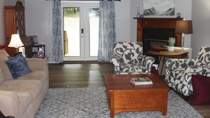 A living room with a sofa, armchairs, a coffee table, a fireplace, and a door leading outside.