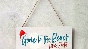 Een rechthoekig bord met een kerstmuts en de tekst 'Gone to the Beach Love, Santa' hangt aan een muur.