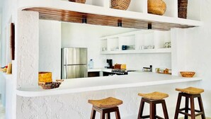 A modern kitchen with white walls, a stainless steel refrigerator, and a bar area with stools.