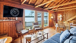 A wooden interior with a television, seating, and a view of the outdoors. - Omena Point Paradise | Waterfront | Sunrise | (Omena)