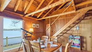 A wooden cabin with a dining table set for four, a telescope, and a bookshelf.