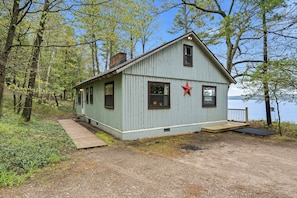 A small, light blue cabin with a red star on the wall, a wooden deck, and a view of a lake. - Omena Point Paradise | Waterfront | Sunrise | (Omena)