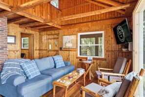 A wooden cabin interior with a sofa, armchairs, a table, and a television.