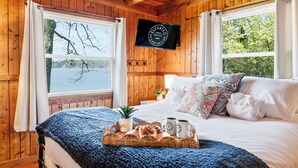 A wooden cabin bedroom with a bed, a TV, a window with curtains, and a breakfast tray.