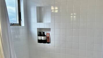 Ein modernes Badezimmer mit weißen Fliesen, einer Badewanne, einem Fenster mit Ausblick und Ablagefläche für Toilettenartikel.
