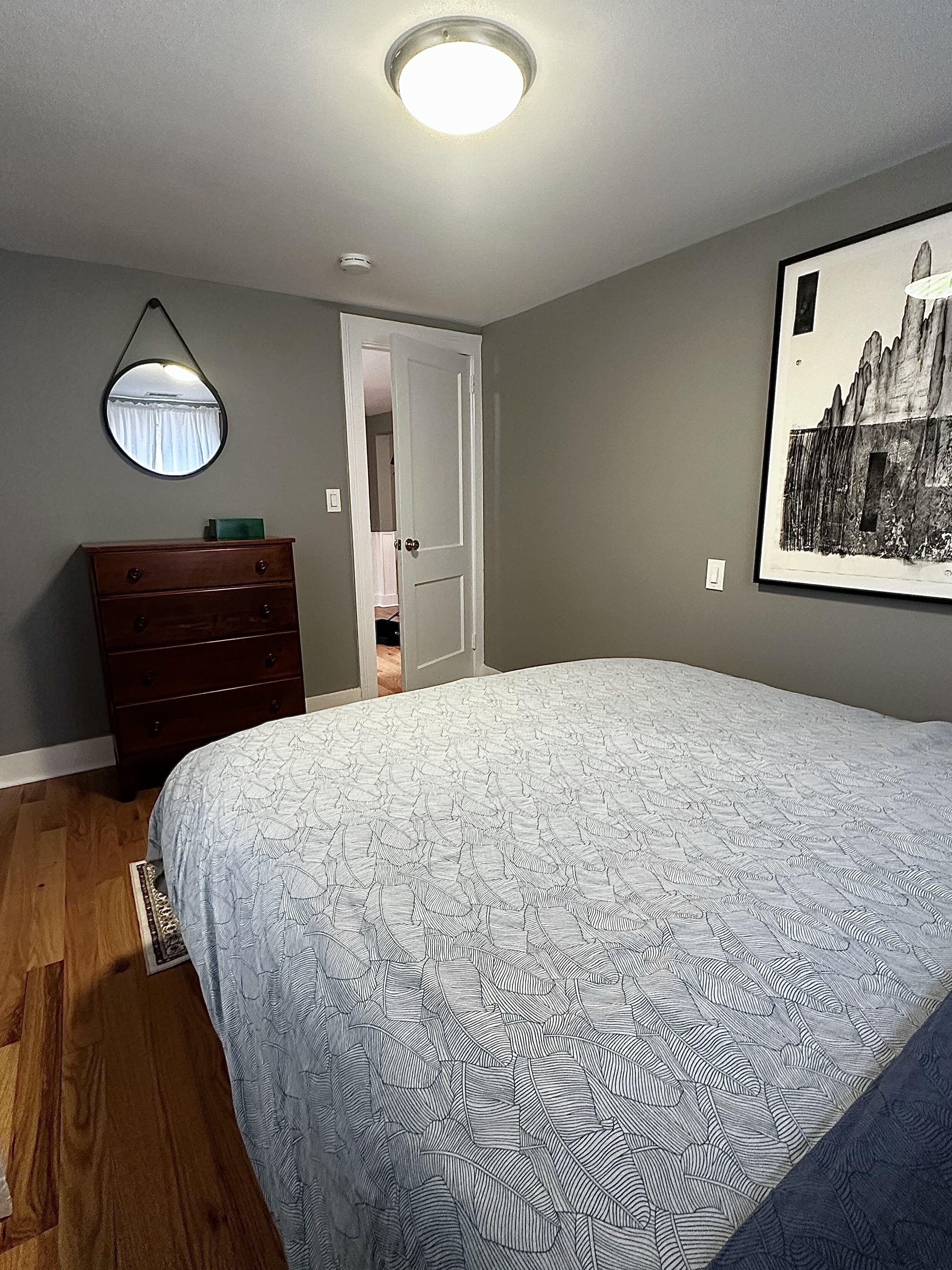 A bedroom with a bed, dresser, and a door leading to another room.