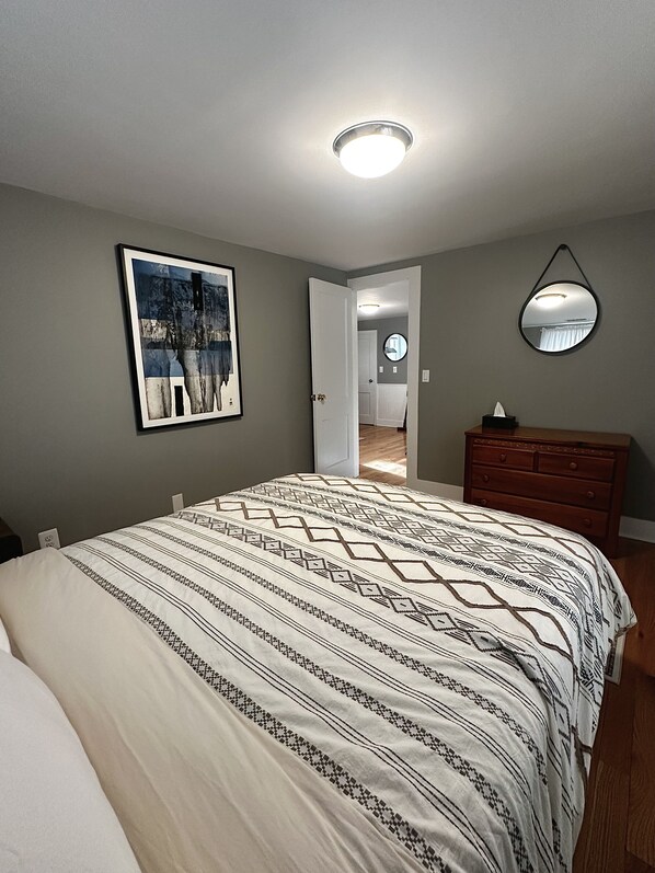 A bedroom with a bed, a dresser, a framed picture on the wall, and a door leading to another room.