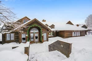 A wooden lodge with a snow-covered roof and a welcoming entrance adorned with greenery. - 2-bedroom condo with weekend shuttle, pool, and hot tub. (Killington)