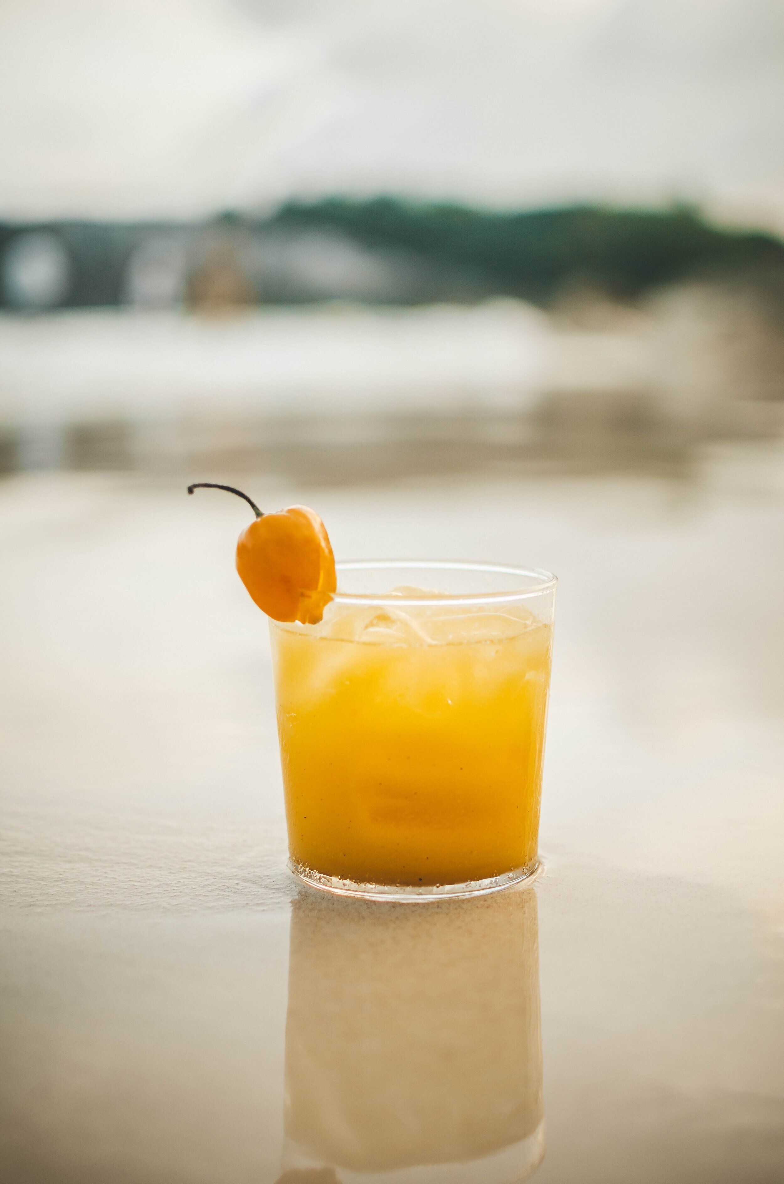 A glass of orange juice with a cherry garnish on a reflective surface.