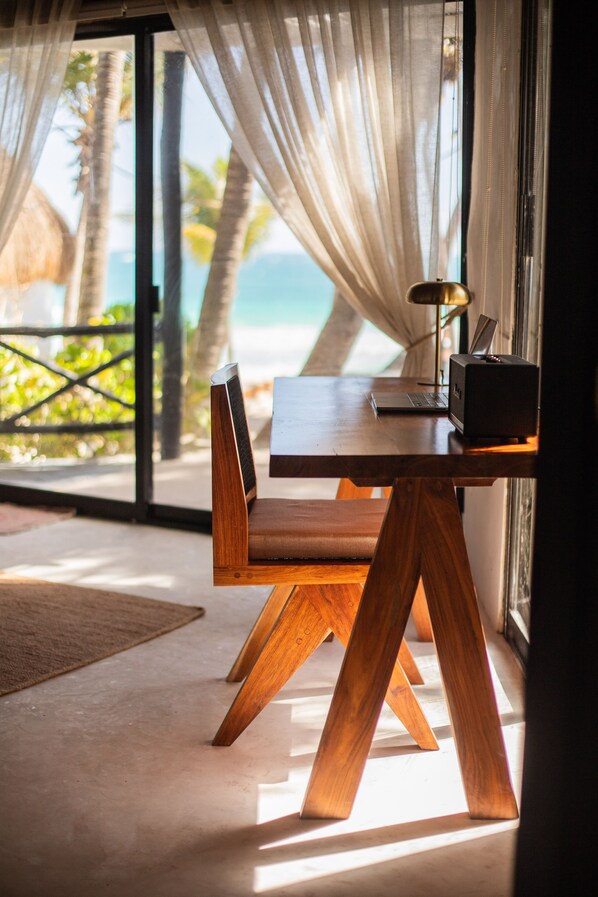 A wooden table with a laptop and a speaker, positioned near a window with sheer curtains. - Casa Gitano (Tulum)