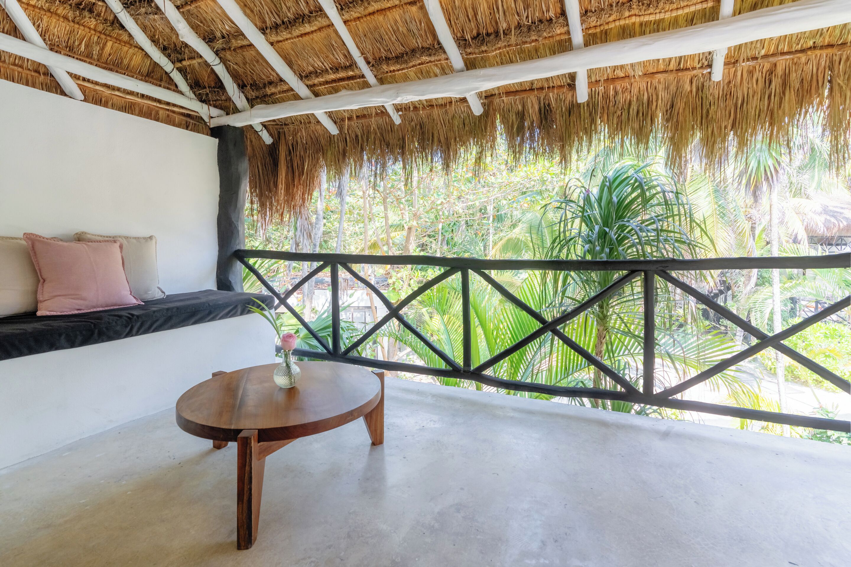 A room with a thatched roof, a balcony with a metal railing, a sofa with cushions, and a small wooden table.
