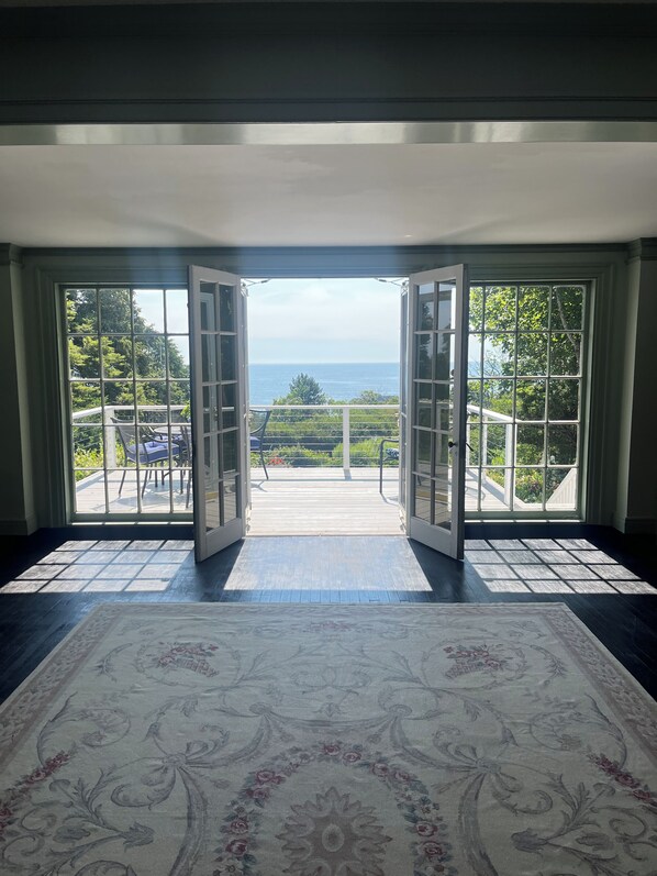Puerta abierta que da a un balcón con vistas al mar y al verdor.