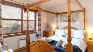 A four-poster bed with a wooden headboard, a bedside table with a lamp, and a window with curtains. - Braeriach by Interhome (Aviemore)