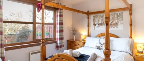 A four-poster bed with a wooden headboard, a bedside table with a lamp, and a window with curtains.
