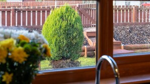 A view through a window with a wooden frame, a metal faucet, and a potted plant with yellow flowers. - Braeriach by Interhome (Aviemore)
