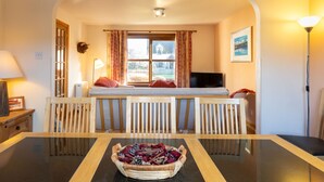 A cozy room with a bed, a TV, a dining table with chairs, and a window with curtains. - Braeriach by Interhome (Aviemore)