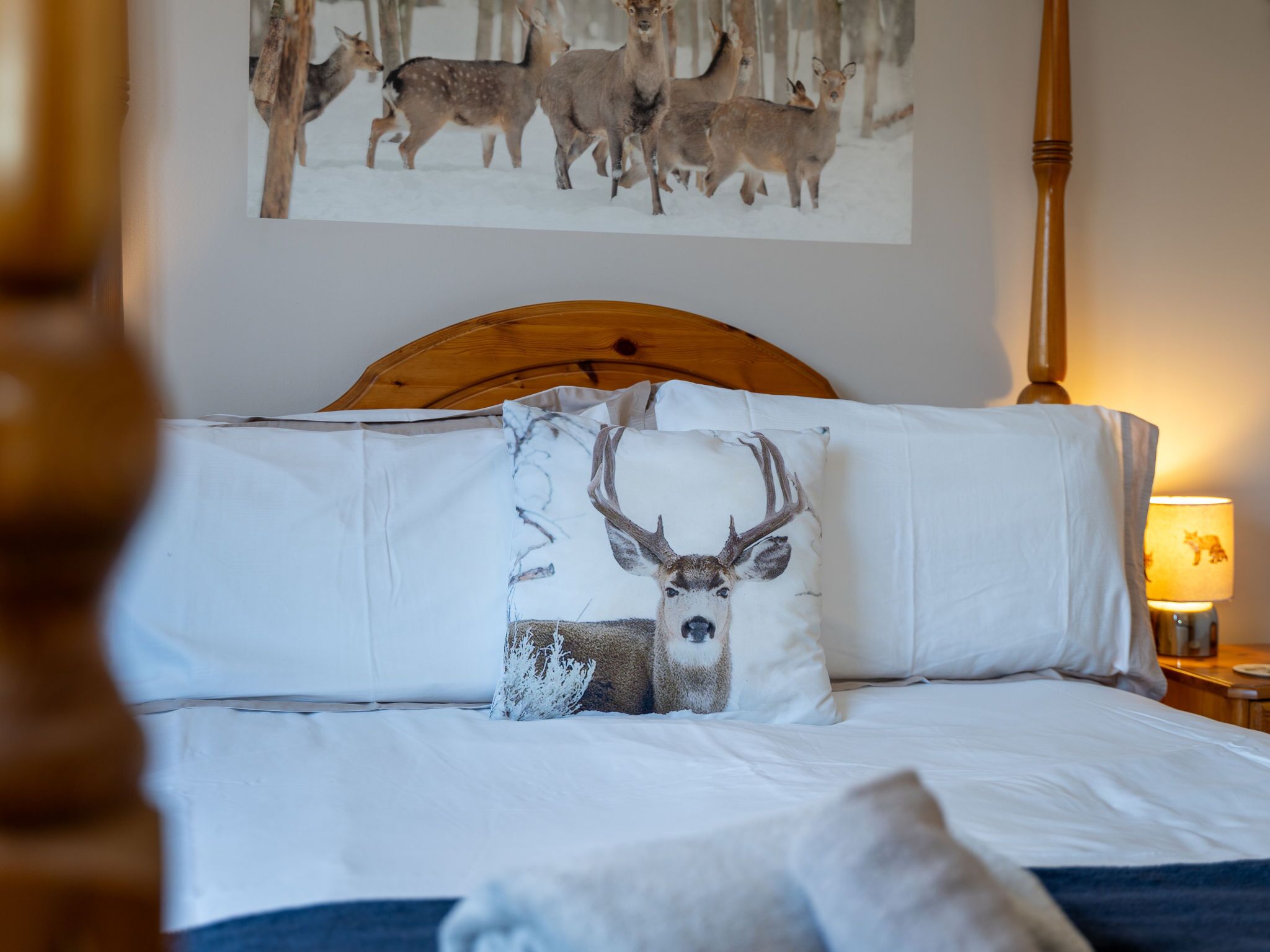 A bed with white linens, a wooden headboard, and decorative pillows including one with a deer.