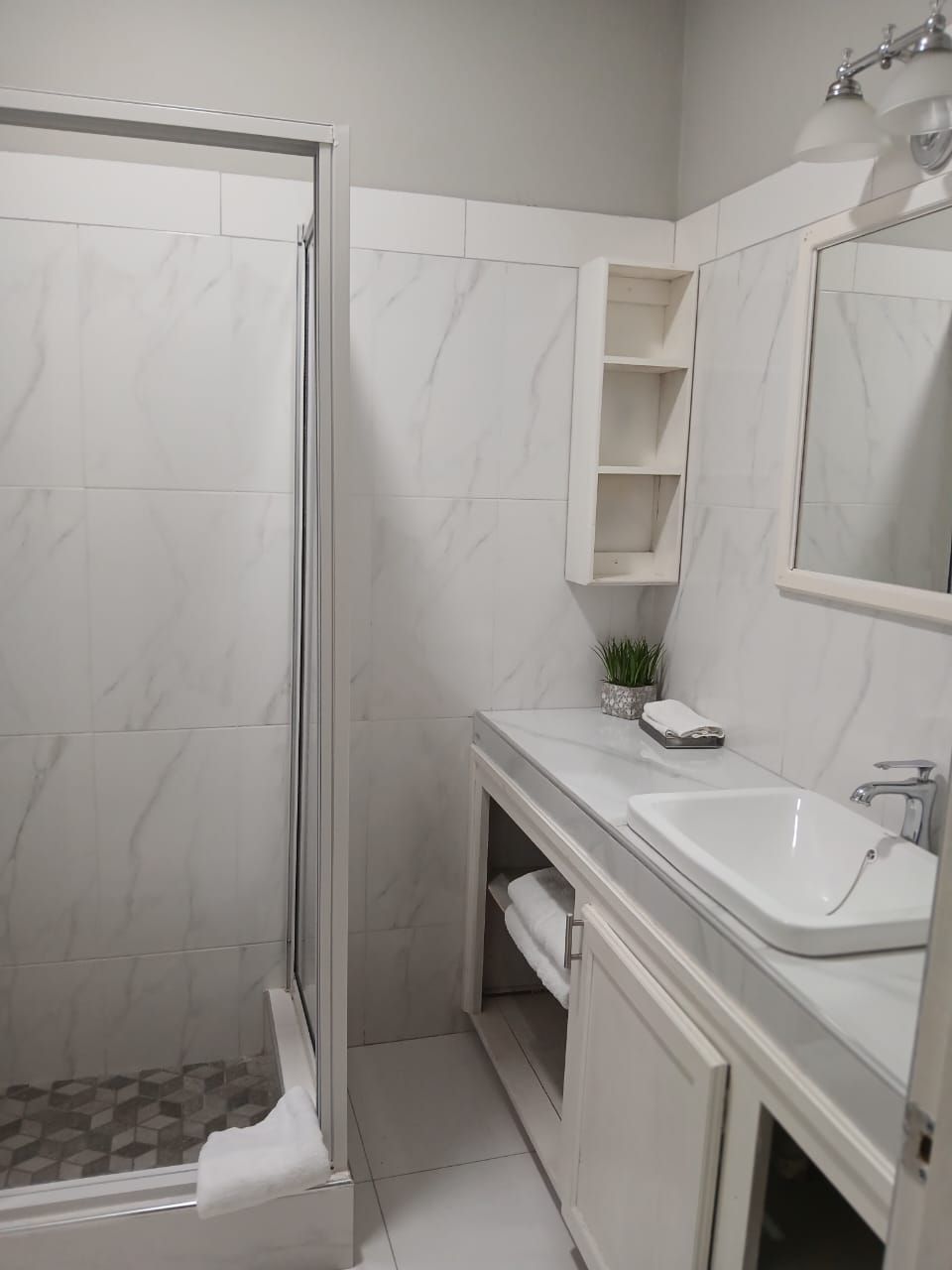 A bathroom with a glass-enclosed shower, a white sink, and a mirror above the vanity.