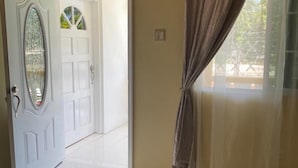 Un dormitorio con una cama, una puerta con panel de vidrio y vista a otra habitación a través de una puerta abierta.