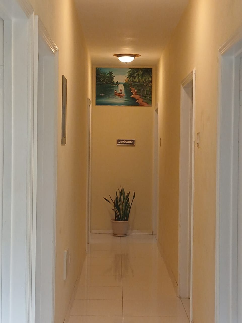 A hallway with a 'welcome' sign, a painting of a boat on water, and a potted plant.