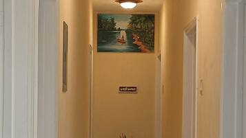 A hallway with a 'welcome' sign, a painting of a boat on water, and a potted plant.