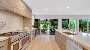 A modern kitchen with a large stove, wooden cabinets, and a view of the outdoor patio. - Heated pool / Lush Tropical Surrounding / Castaway Key / RESlDENCES (Fort Lauderdale)