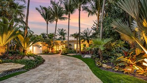 A paved pathway leading to a building with a well-maintained garden and palm trees. - Heated pool / Lush Tropical Surrounding / Castaway Key / RESlDENCES (Fort Lauderdale)