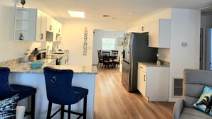 Una cocina moderna con gabinetes blancos, una isla central con taburetes, un refrigerador y un comedor con sillas y una mesa.