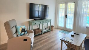Una sala de estar con sofá, televisión, una mesita y una ventana con cortinas.