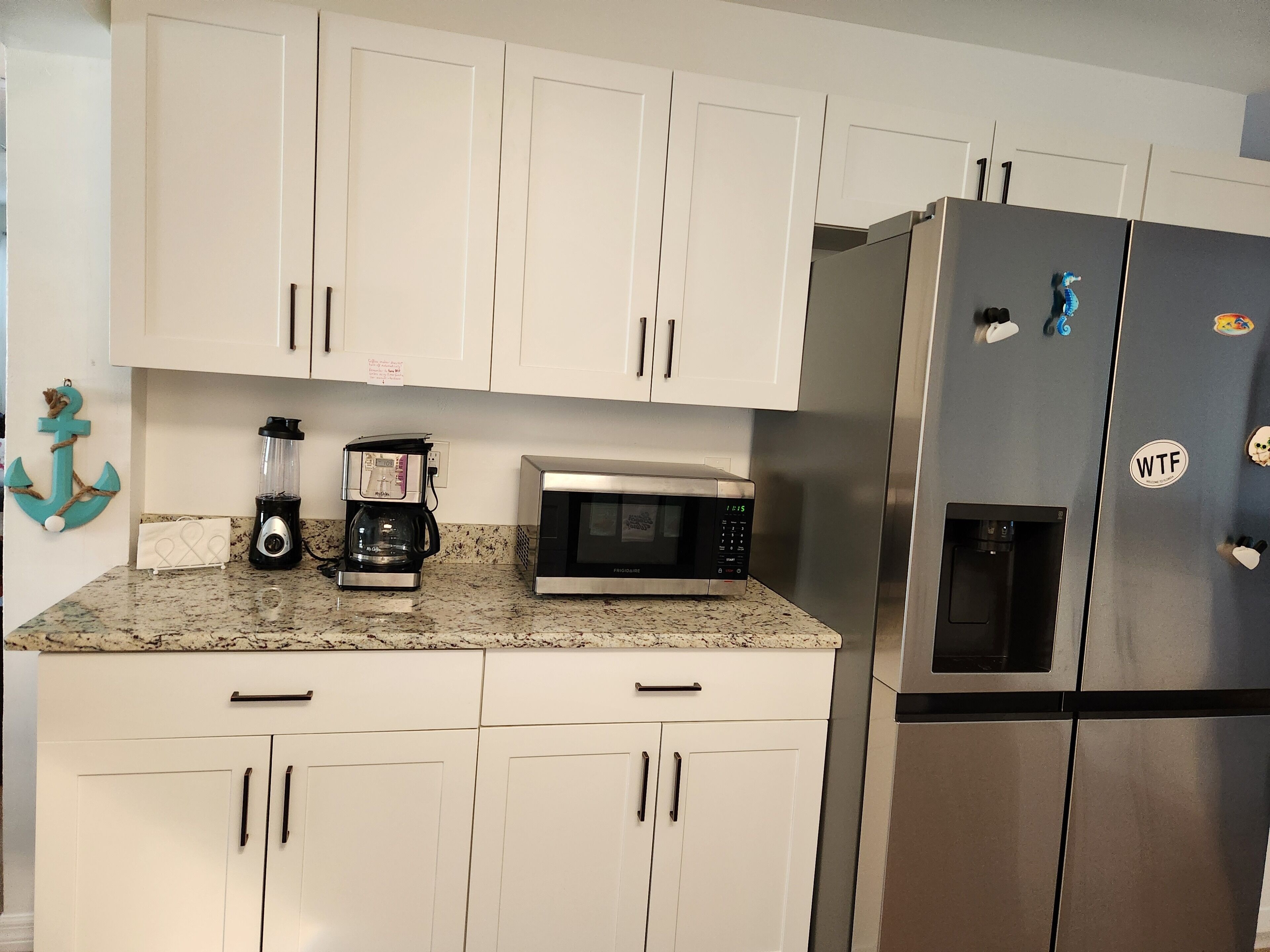 A kitchen with white cabinets, a coffee maker, a microwave, and a refrigerator.
