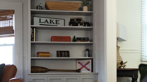 Een kamer met een witte inbouwboekenplank, een bruine lederen fauteuil en een houten bankje.
